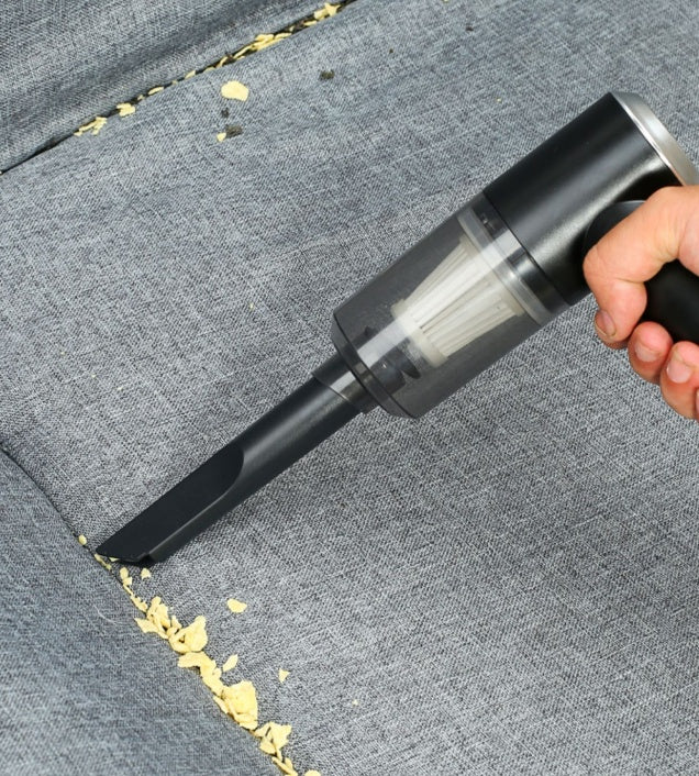 Aspirateur à main ramassant des miettes sur un tapis de voiture
